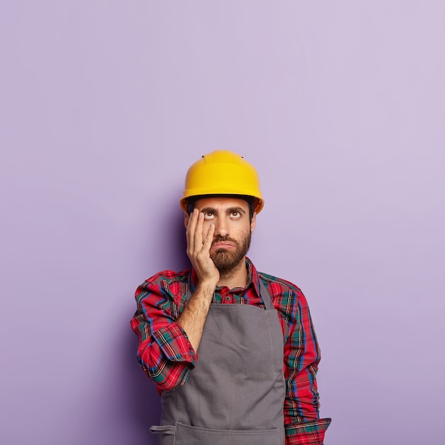 Tired industrial worker wears yellow hardhat and apron