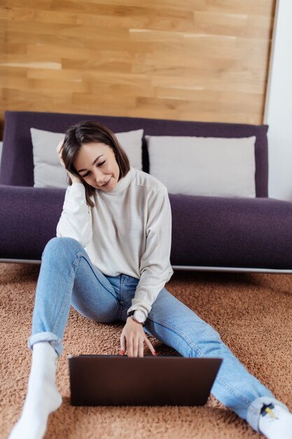 Tired lady works on laptop computer sitting on the floor at home in day time casual dressed