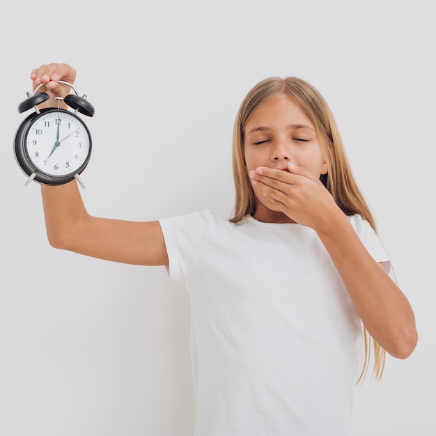 Tired little girl holding a clock up