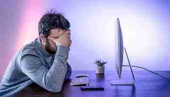 Free photo a tired man sits in front of a computer covering his face with his hands