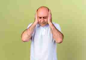 Free photo tired mature man cowered ears with hands isolated on olive green wall