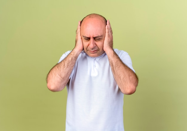 Tired mature man cowered ears with hands isolated on olive green wall