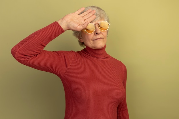 Tired old woman wearing red turtleneck sweater and sunglasses touching head with closed eyes 