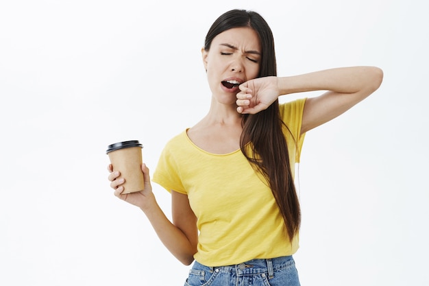 Tired and sleepy cute female coworker in yellow t-shirt yawning with closed eyes covering opened mouth