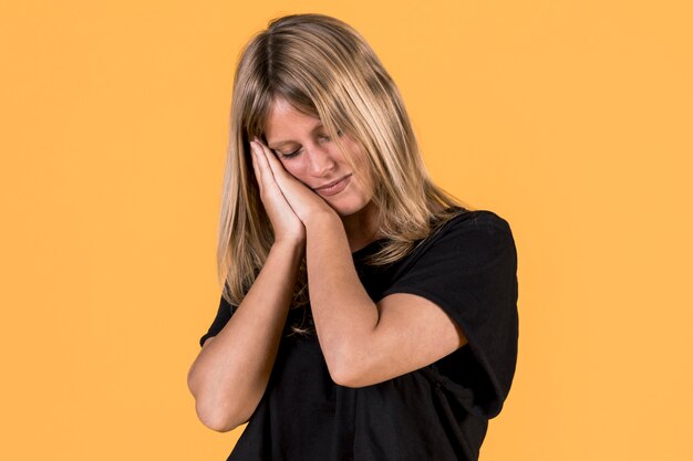 Tired sleepy woman takes nap lean on her palm in front of yellow backdrop