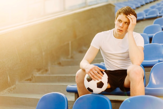 Tired sportsman with ball on stadium