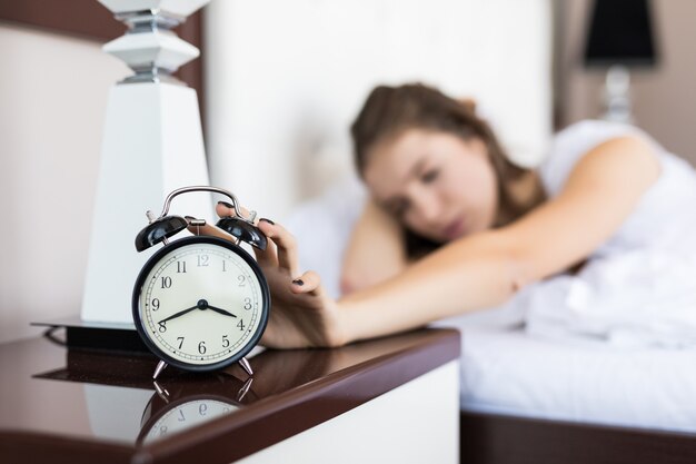 Tired student business girl wake up in the morning due alarm clock ringing in bedroom