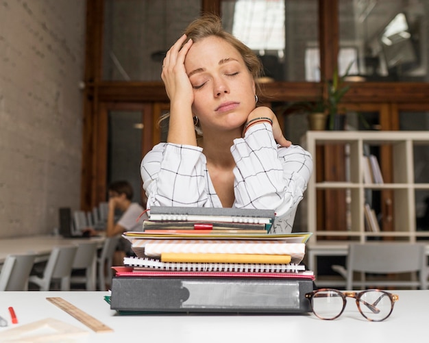 Free photo tired teacher with stack of books on desk