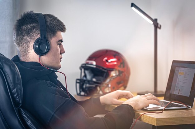 A tired teenager guy in headphones sits in front of a laptop in his room