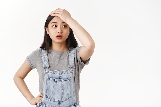 Tired tensed brunette asian girl bothered face troublesome situation touch forehead pressured look aside sighing exhausted worry cannot deal lots work standing white background