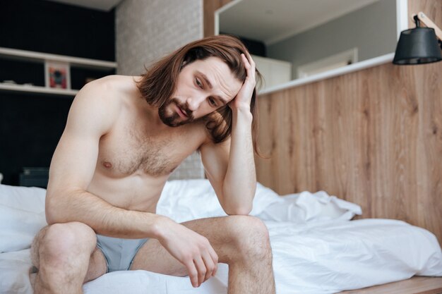 Tired thoughtful young man sitting and thinking on bed