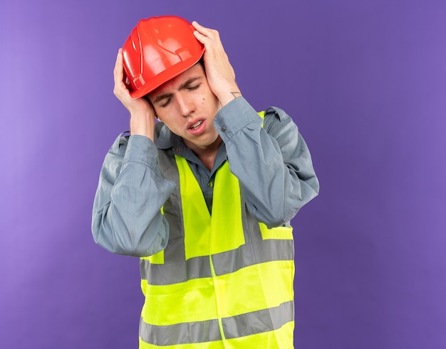 Free photo tired with closed eyes young builder man in uniform grabbed head