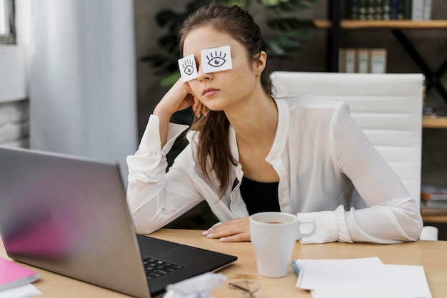 Free photo tired woman covering her eyes with drawn eyes on paper