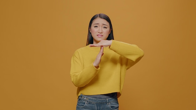 Tired woman doing timeout and break gesture in studio, expressing t shape sign with hands to pause action. Serious person gesticulating refuse and need to finish. Concept of restriction