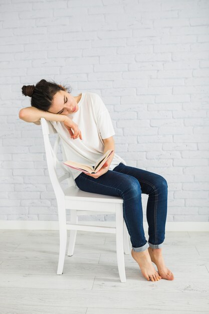 Tired woman reading book on chair
