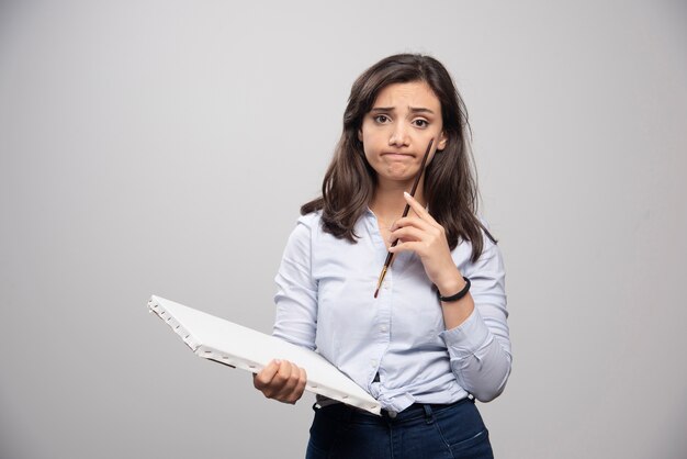 Tired woman standing on gray wall with canvas and brush. 