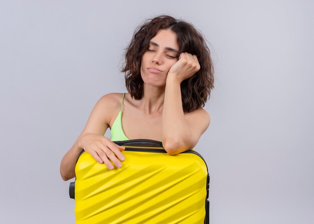 Tired young beautiful traveler woman holding suitcase on isolated white wall