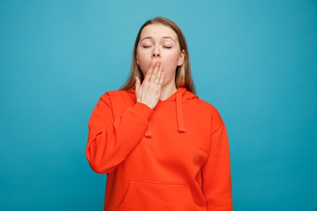 Tired young blonde woman yawning keeping hand on mouth with closed eyes 