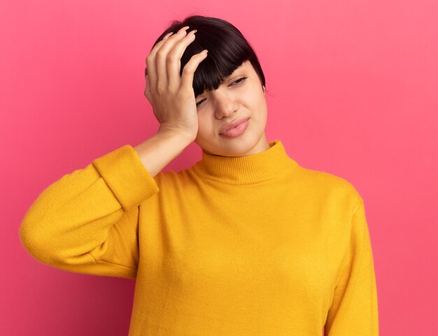 疲れた若いブルネットの白人の女の子は頭に手を置き、横を見る