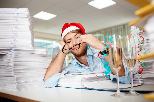 クリスマスの日の論文の中で職場に座って疲れている青年実業家。