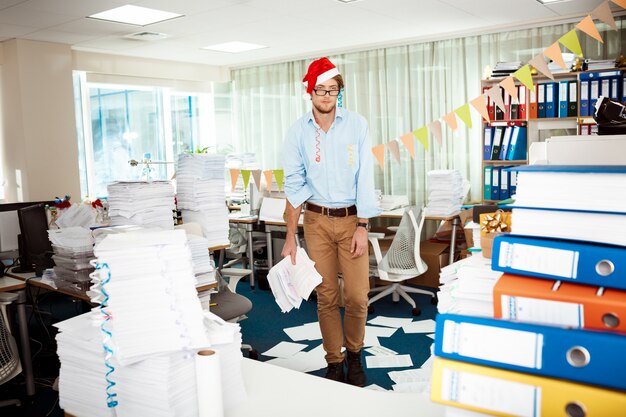 Tired young businessman working in office among papers on christmas day.