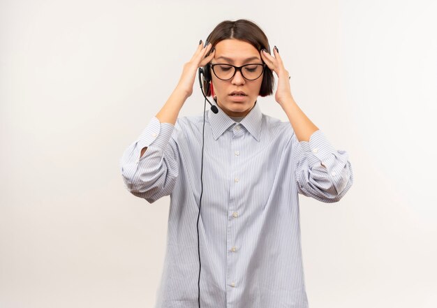 Tired young call center girl wearing glasses and headset putting hands on temples with closed eyes isolated on white wall