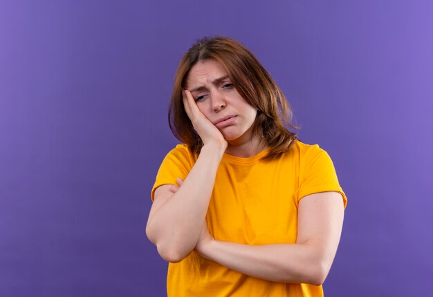 Tired young casual woman putting hand on cheek on isolated purple wall with copy space