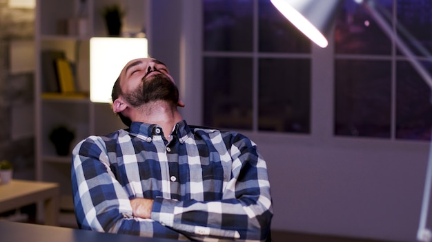 Tired young caucasian entrepreneur sleeping on chair in his home office. Overworked businessman.