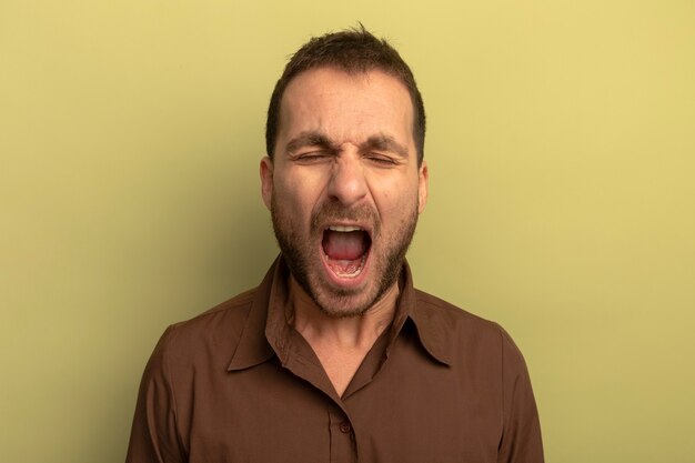 Tired young caucasian man yawning with closed eyes isolated on olive green background