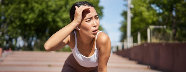 Tired young female runner asian girl taking break during workout stop jogging panting while