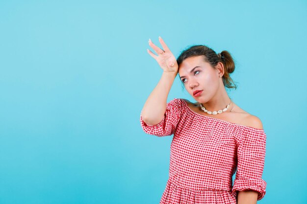 Tired young girl is holding hand on forehead on blue background