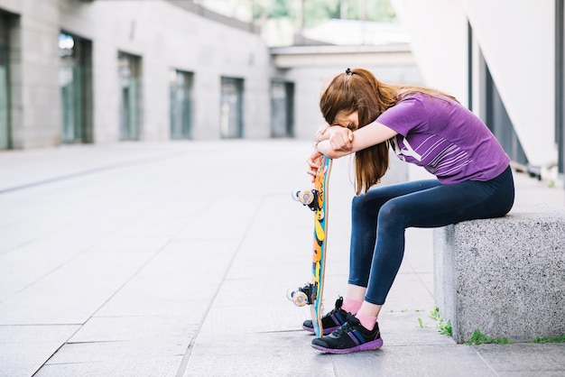 Foto gratuita ragazza stanca con lo skateboard si siede sul bordo