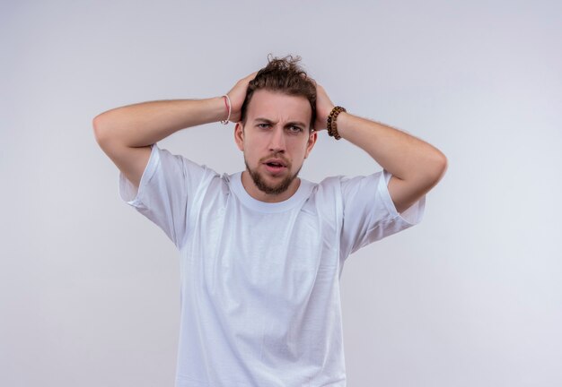 Tired young guy wearing white t-shirt grabbed head on isolated white wall