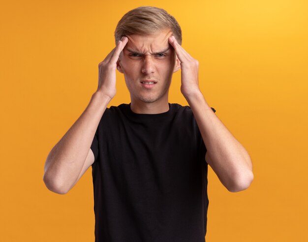 Tired young handsome guy wearing black shirt putting hands on forehead isolated on yellow wall