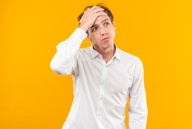 Tired young handsome guy wearing white shirt putting hand on forehead isolated on orange wall