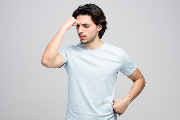 tired young handsome man touching head with fist and touching waist with closed eyes isolated on white background