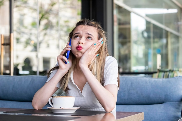 Tired young lady talking on the phone and sitting at the restaurant