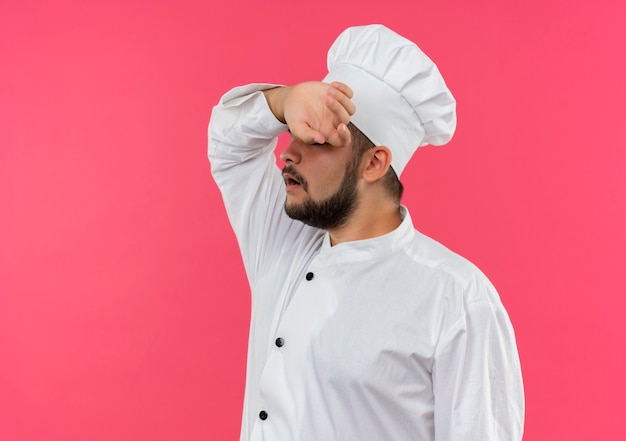 Foto gratuita cuoco maschio giovane stanco in uniforme del cuoco unico che mette la mano sulla fronte isolata sullo spazio rosa