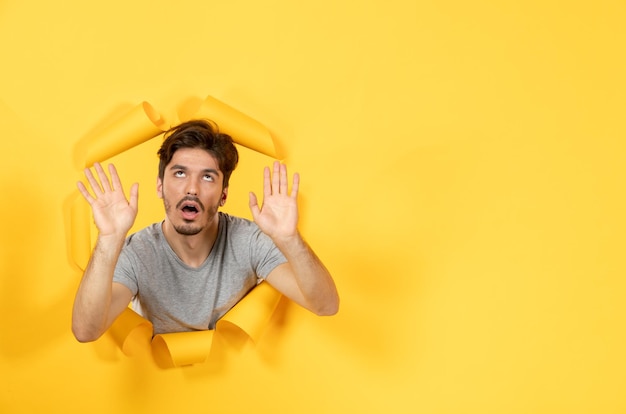 Tired young male looking from torn yellow paper surface