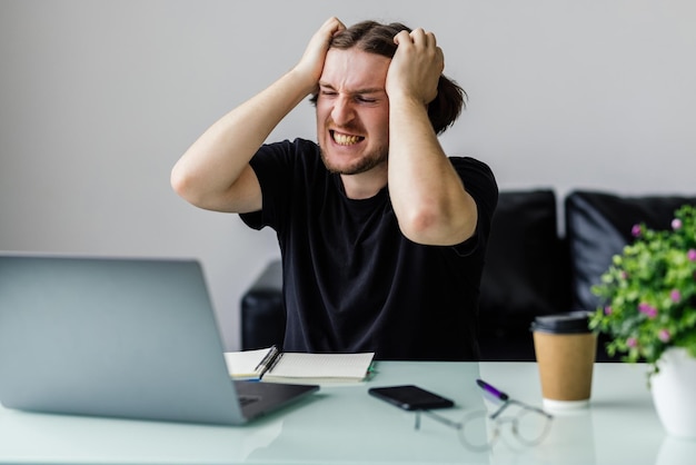 Tired young man feel pain eyestrain holding glasses rubbing dry irritated eyes fatigued from computer work stressed man suffer from headache bad vision sight problem sit at home table using laptop