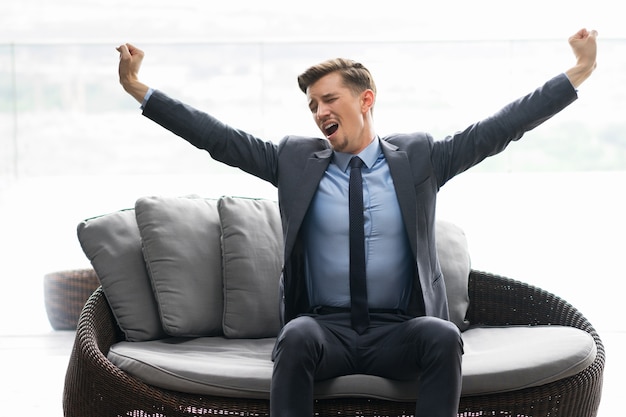 Tired Young Man Sitting on Couch and Yawning