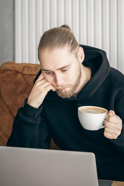 Tired young man working on a laptop with a cup of coffee