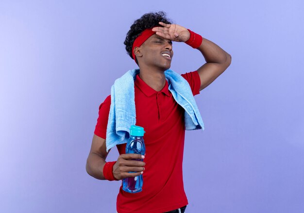 Tired young sporty man wearing headband and wristband putting hand