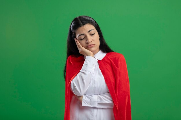 Tired young superwoman holding her chin with hand and napping on feets with closed eyes on green walls