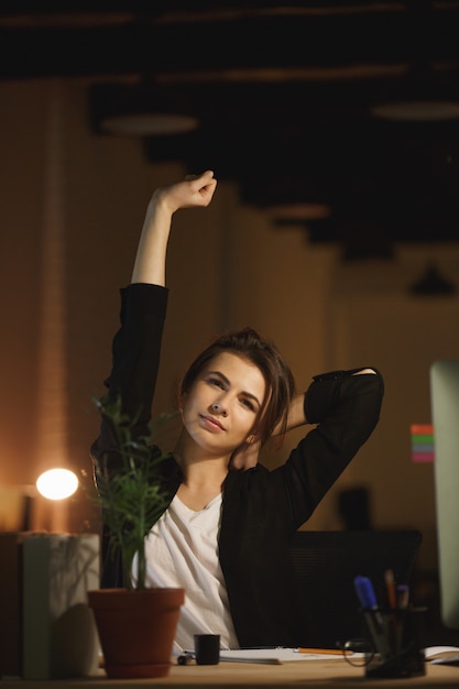 Tired young woman designer sitting in office at night