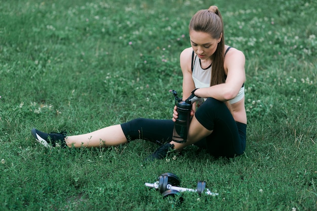 Бесплатное фото Усталая молодая женщина после тренировки опирается на зеленую траву