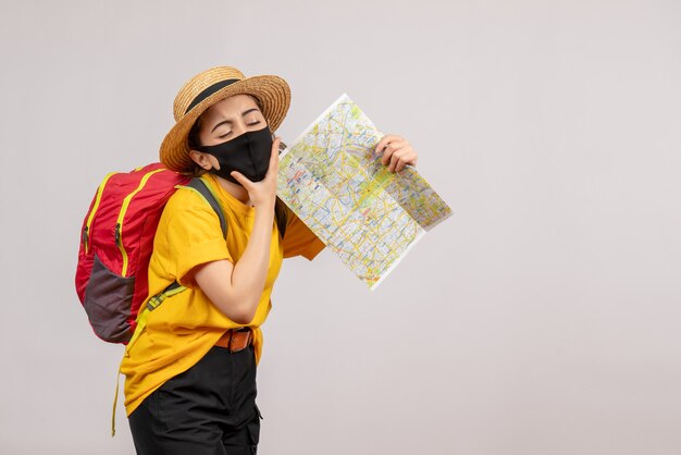 tired young woman with red backpack holding up map on grey