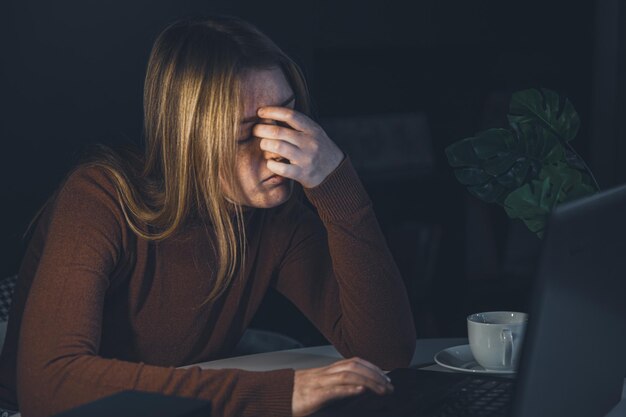 夜の病気の目のラップトップの後ろで働く疲れた若い女性