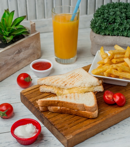 Toast sanwdiches with cheese inside with fries, tomato sauce and glass of orange juice.