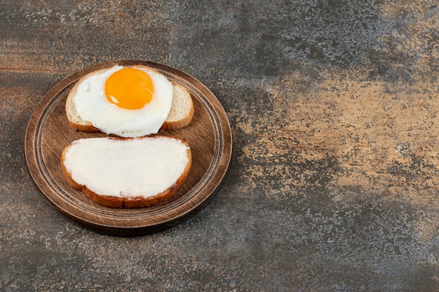 Toast with cream cheese and egg on wooden board.